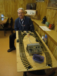 James sitting behind the demonstration track highlighting the semaphores and interlocking detectors that control starting and stopping the trains as well as the turnouts.